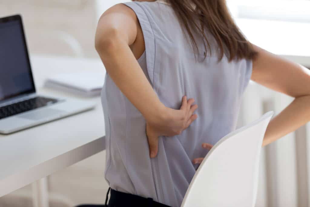 femme assise au travail devant son ordinateur se tenant le dos à cause des douleurs
